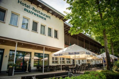 a hotel with tables and umbrellas in front of a building at Hotel Russweiher in Eschenbach in der Oberpfalz