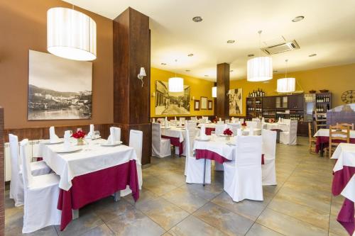 un restaurante con mesas y sillas blancas y lámparas de araña en Hostal Restaurante Alarico en Allariz