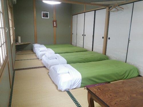a room with a row of beds with green sheets at Miyoshino Sakuraan in Yoshino