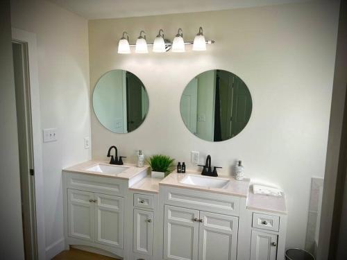 a bathroom with two sinks and two mirrors at Coastal Escape: Sleek King Suite on Half Acre in Gulfport