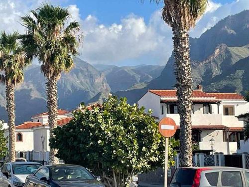 una calle con coches aparcados, palmeras y montañas en Villa Garoe, en Puerto de las Nieves