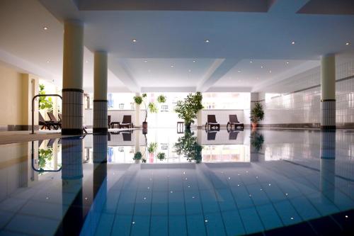 a swimming pool in a building with tables and chairs at Sonnenhotel Fürstenbauer in Bodenmais