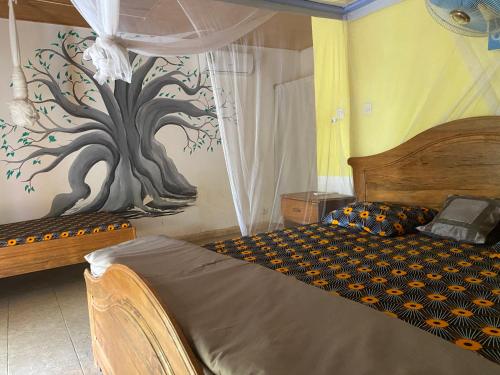 a bedroom with a bed with a tree painted on the wall at La kora in Toubakouta