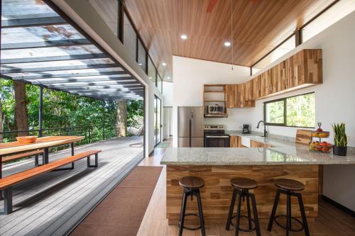 an open kitchen with wooden cabinets and a large island with bar stools at Casa Henaway - Portasol Vacation in Savegre