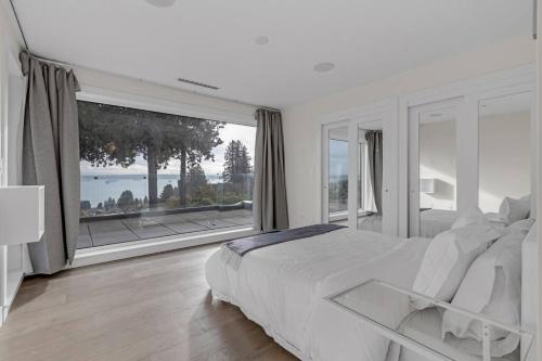 una camera bianca con un grande letto e una grande finestra di Modern Home with Breathtaking Ocean & City Views a West Vancouver