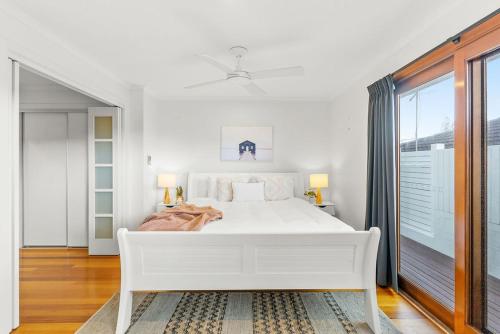 a white bedroom with a white bed and a window at Beach House in Lennox Head