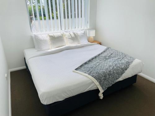 uma cama com lençóis e almofadas brancos e uma janela em Modern City Townhouse with all the Comforts em Wagga Wagga
