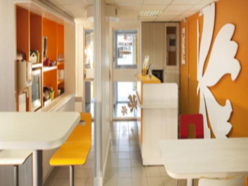 a kitchen with orange walls and a white table and chairs at Premiere Classe Auxerre in Monéteau