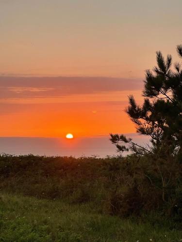 a sunset over the ocean with a tree in the foreground at El Rancho Busto - Luarca in Busto
