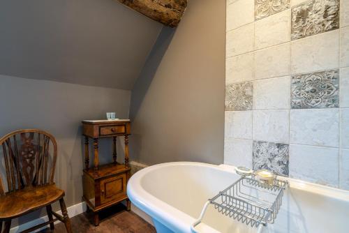 a bathroom with a tub and a wooden chair at Broughwood Cottage Snowshill in Broadway