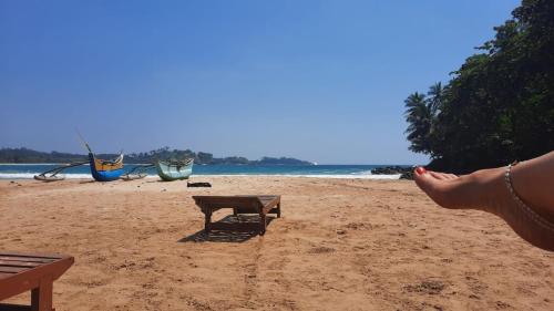 a person sitting on a beach with a bench and boats at Talalla Wonder View in Talalla South