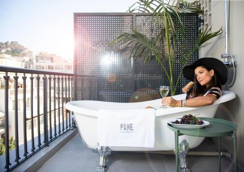 una donna seduta in una vasca da bagno su un balcone di PAME Paradiso ad Atene