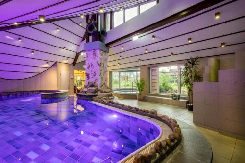 a swimming pool in a building with purple lighting at Ringhotel Köhlers Forsthaus in Aurich