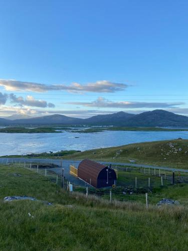 a barn on a hill next to a body of water at Meall Ard Self Catering Pod - Isle of South Uist in Pollachar