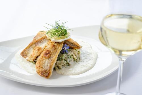 a white plate with a sandwich and a glass of wine at Köhlers Forsthaus Wellness & Genuss Hotel in Aurich