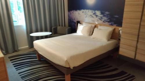 a hotel room with a bed with white sheets and pillows at Novotel Valence Sud in Valence