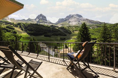 une personne assise sur une chaise sur un balcon avec des montagnes dans l'établissement Belambra Clubs Gourette - Lou Sarri, à Gourette