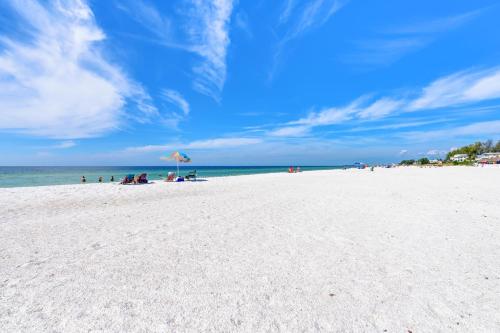 a white beach with people sitting under an umbrella at Absolute Anna Maria-Private Beach Access-Heated Pool-Water Views From Every Room in Bradenton Beach