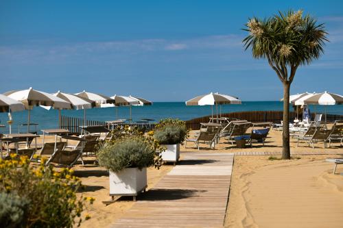 una playa con sillas y sombrillas y el océano en Savoy Beach Hotel & Thermal Spa en Bibione