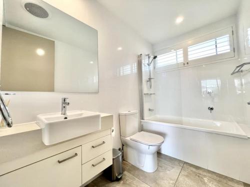 La salle de bains blanche est pourvue d'un lavabo, de toilettes et d'une baignoire. dans l'établissement 6Apt Beautifully renovated on Hastings Street, à Noosa Heads