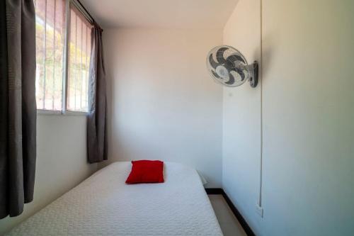 a small bedroom with a white bed with a red pillow at Hotel Cabañas Villa Roca, Rodadero in Santa Marta