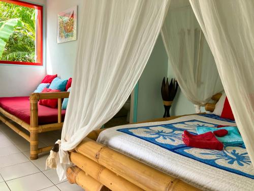 a bedroom with a bed with white curtains and red pillows at Gîte Zandoli Koko in Sainte-Anne