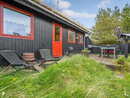 a black house with red doors and chairs and a table at Holiday Home Kathaline - 3-4km from the sea in Western Jutland by Interhome in Bolilmark