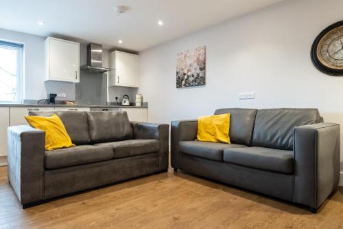 two leather couches with yellow pillows in a living room at James Charles Apartments in Milton Keynes