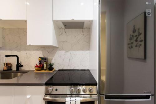 a kitchen with white cabinets and a stainless steel refrigerator at Palms Little Italy Studio with full bathroom by Denstays in Montréal