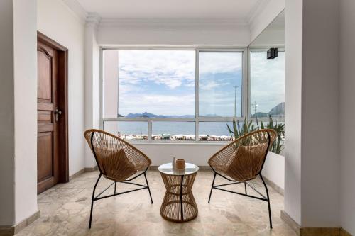 Duas cadeiras e uma mesa num quarto com uma grande janela em Sofisticado em Copacabana - Vista para praia - A403 Z3 no Rio de Janeiro