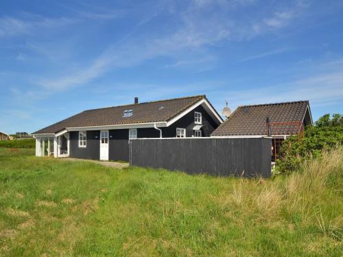een zwart-wit huis met een hek in een veld bij Holiday Home Jerker - 400m from the sea in NW Jutland by Interhome in Løkken
