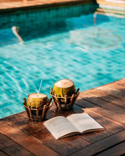 two melons in baskets and an open book next to a swimming pool at Jubarte Hotel by Insólito in Búzios
