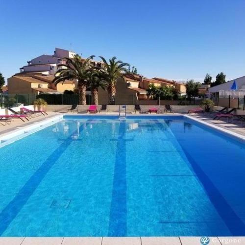 une grande piscine bleue avec des palmiers et un bâtiment dans l'établissement Naturiste Port Soleil, au Cap d'Agde