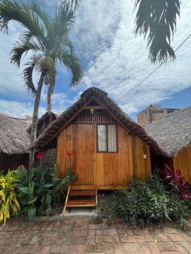 a wooden house with a thatched roof and a palm tree at Zutalu - Playa Sur in Puerto López