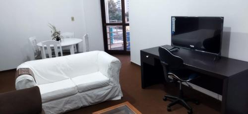 uma sala de estar com uma secretária, uma televisão e uma cadeira em Praça Residence em Uruguaiana