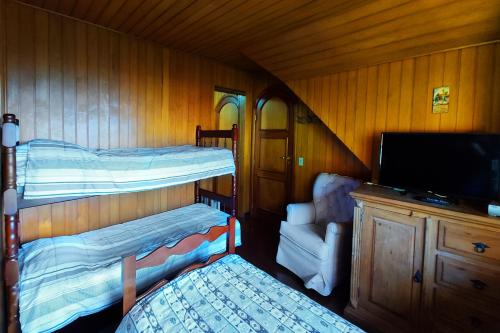 a room with two bunk beds and a tv and a chair at Pousada Casa dos Sonhos in Campos do Jordão