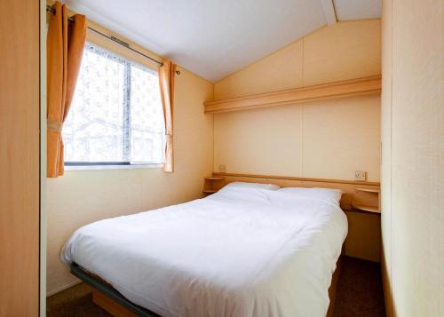 a small bedroom with a white bed and a window at Eastern Beach Caravan Park in Caister-on-Sea