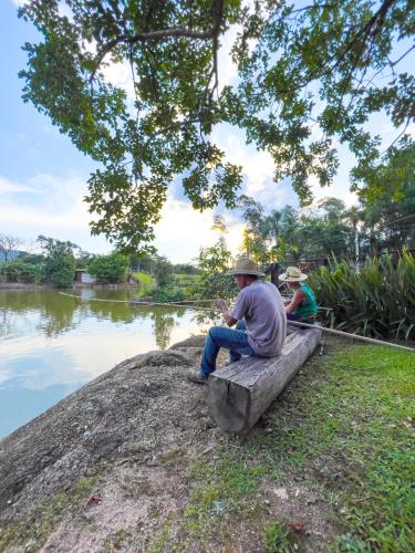 a man sitting on a bench next to a river at Seu Refúgio Rural Piscina Privativa e Natureza in Tubarão