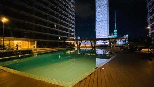 Cozy 1Br with Netflix & Balcony Pool View Condo في مانيلا: حمام سباحة في الليل مع مبنى طويل