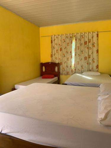 Duas camas num quarto com paredes amarelas e uma janela em casa rural Bon Tempo em Pirenópolis