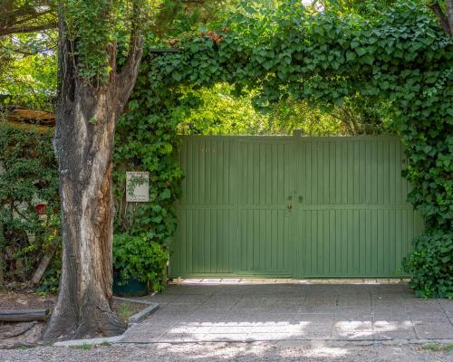 una puerta verde de garaje con un árbol delante en Alquiler temp "UNA PAUSA" Barrio Privado en Vistalba en Mendoza