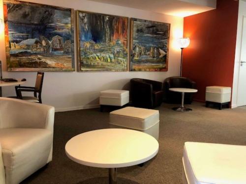 a waiting room with chairs and tables and paintings on the wall at Hôtel Le Palladior Voiron in Voiron