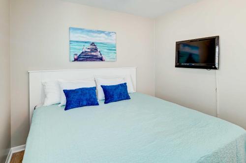 a bedroom with a bed with blue pillows and a tv at Murrells Inlet Condo on Garden City Beach! in Myrtle Beach