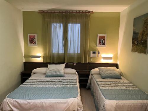 2 Betten in einem kleinen Zimmer mit Fenster in der Unterkunft Hostal La Vila in Olot