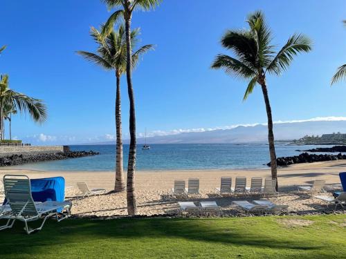 a beach with chairs and palm trees and the ocean at Mauna Lani Palm Villas D-2 Corner Unit Historic View in Waikoloa
