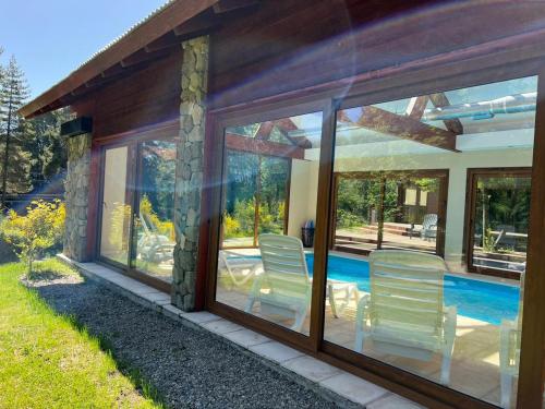 a house with glass doors and chairs next to a swimming pool at Solar Selvana - Casas de montaña in Villa La Angostura
