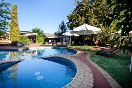 uma grande piscina com um guarda-sol e um pátio em Mercure Port of Echuca em Echuca