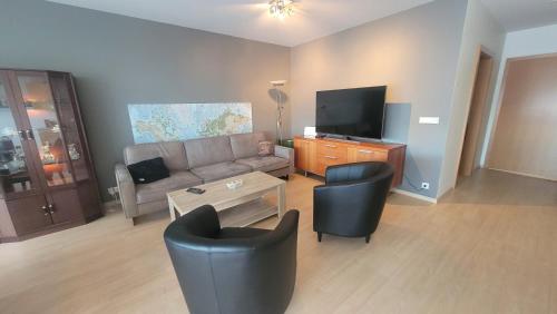 a living room with a couch and a tv and chairs at Bright appartment in Egilsstadir