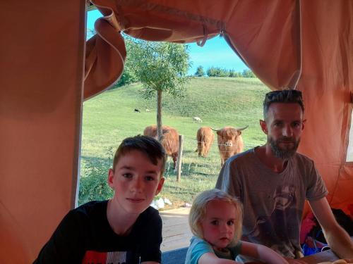 mężczyzna i dwoje dzieci siedzących w namiocie z krowami w obiekcie Sheepinn de geul w mieście Tielt