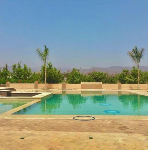 a swimming pool with blue water and palm trees at Tanazart guest house in Taroudant